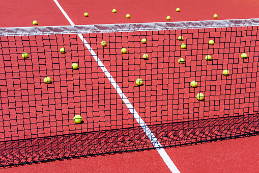 MANY TENNIS OR PADEL BALLS SCATTERED ON THE COURT NEXT TO THE NET. TRAINING CONCEPT. SPORT BETS IN BETTING SHOPS.