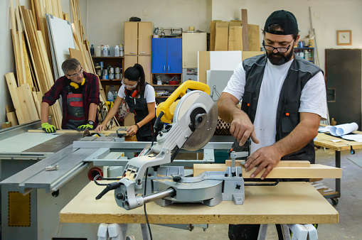 A Workers in Carpentry Workshop are Measuring a Timber Plank and Prepare to Cut it with an Electric Circular Saw.