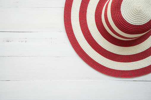 Large red lady hat on white wooden background with copy space. Travel summer beach holiday, airline and hotel business concept.