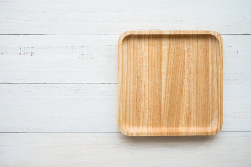 Top view of unused new brown handmade wooden dish plate on white wooden table background. Kitchen utensil, food concept.