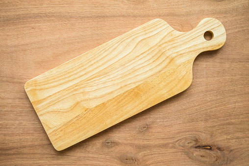 Top view of unused new brown handmade wooden cutting board on wooden table background. Cooking, kitchen utensil, food restaurant concept.