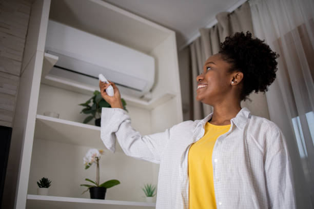 Young woman turning on air conditioner
