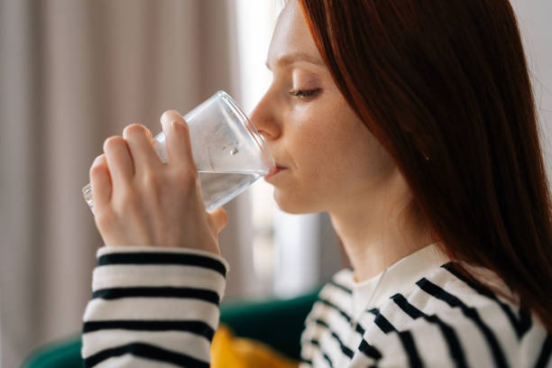 Close-up face of pretty redhead female drinking still water at home. Concept of quench thirst, water balance and weight control, caring of skin and body Close-up face of pretty redhead female drinking still water at home. Concept of quench thirst, water balance and weight control, caring of skin and body, hangover relief, body refreshment. quench your thirst pictures stock pictures, royalty-free photos & images