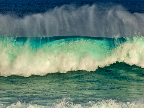 Close-up of a big wave breaking against rocky ledges in the sea