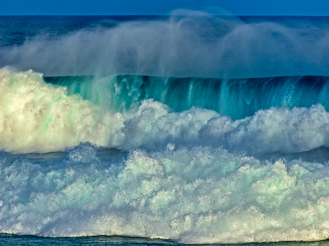 Powerful ocean water crashing on high rocky seashore with huge splashes at summer sunlight. Aerial view stormy dangerous sea waves hitting coastal cliffs slow motion. Amazing power of ocean surf.