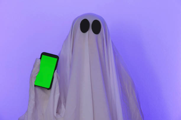 The ghost shows a phone with a green screen. Phone with chromakey. The ghost makes an order from smartphone on Halloween. Free space. The ghost poses with the phone.