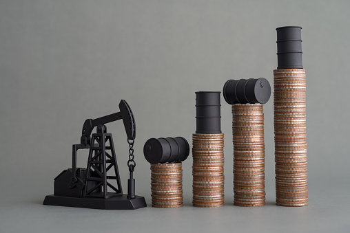 Crude oil tank on stack coin as price chart graph rising up and pump jack on grey background. World petroleum and energy industry or trading commodity investment, crude oil and gas price increase concept
