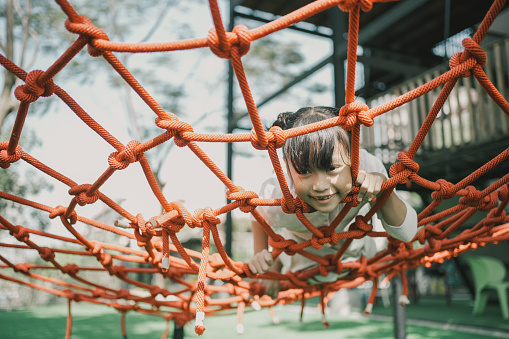 Primary mixed Asian girl having fun on Spiderweb Climbing Net, outdoor activity at school playground