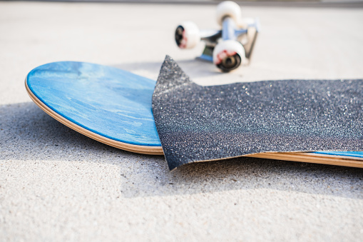 Applying grip tape to a brand new skateboard deck next to a set of trucks and wheels