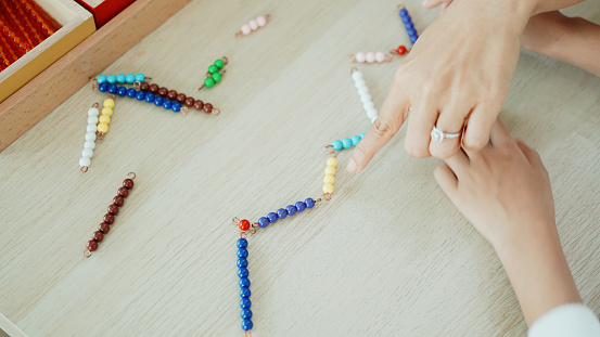 Elementary girl counting color bead chain to learn mathematics in Montessori education school and homeschooling