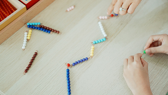 Elementary girl counting color bead chain to learn mathematics in Montessori education school and homeschooling