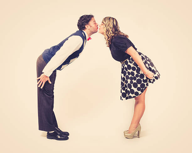 a young male and young female lean in to kiss each other. retro feel against a clean backdrop.