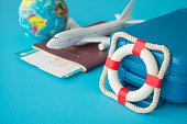 Lifebuoy safe suitcase travelers, passport, flight tickets, airplane and globe on blue background.