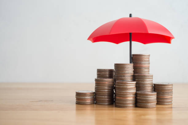 istock Stacked coins is protected by red umbrella on wooden table white wall background. 1617692100