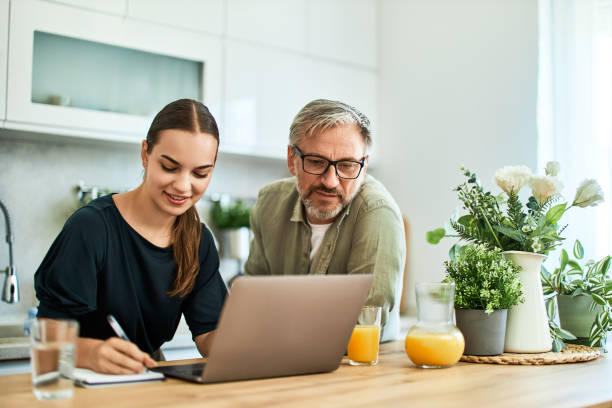 istock A smiling woman writes notes while using a laptop with her father at home. 1617700731
