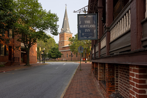 Annapolis, Maryland, USA - June 30, 2023: Duke of Gloucester Street with sidewalks paved by red bricks in Annapolis. The Maryland Inn nameplate on the building is the Historic Inns of Annapolis, MD. St. Anne's Parish Church view in the distant