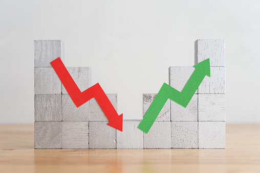 Wood block bar graph and arrow red green chart volatility up and down on wooden table white wall background. Business, financial and investment concept. Risk, fluctuation in stock market and cryptocurrency.