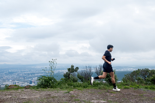 A man embraces the highland beauty of Cimatario, Queretaro, running amidst clouds, trees, and mountains, a perfect blend of nature and endurance