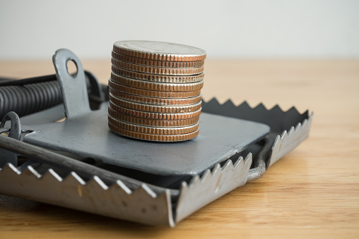 Close up stacked coins in danger a mousetrap on wooden background. Online internet financial scam, internet fraud, phishing email hacker, swindler, gambling, online betting or offline scam concept.