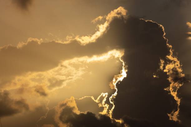 istock Bright golden sun peeking through fluffy white clouds 1617860194
