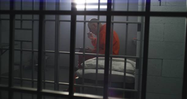 istock Elderly prisoner sits in prison cell in jail, eats food 1617861850