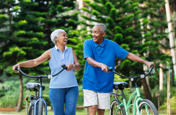 Senior African American couple walk with bikes, laughing
