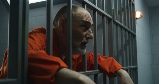 istock Upset inmate stands behind bars in jail or correctional facility 1617879578
