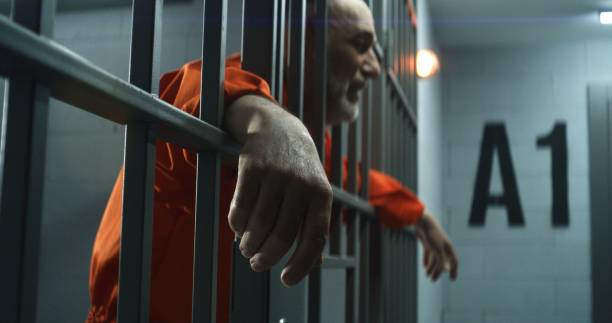 istock Upset inmate stands behind bars in jail or correctional facility 1617880137