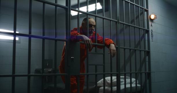 istock Prisoner in orange uniform leans on metal bars 1617889744