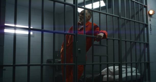 istock Prisoner in orange uniform leans on metal bars 1617891799