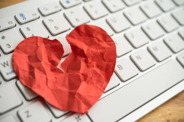 Red broken heart paper on white keyboard computer background. Red broken heart paper on white keyboard computer background. Online internet romance scam or swindler in website application dating concept. Love is bait or victim. Romance stock pictures, royalty-free photos & images