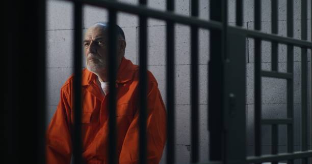 istock Criminal in orange uniform sits on prison bed 1617898287
