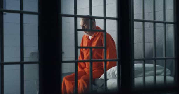 istock Criminal in orange uniform sits on prison bed 1617901955