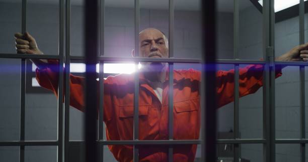 istock Elderly prisoner holds hands on metal bars 1617903506