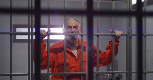 istock Elderly prisoner holds hands on metal bars 1617904544