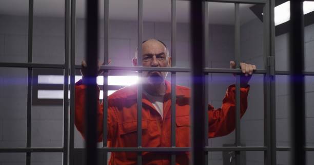 istock Elderly prisoner holds hands on metal bars 1617904618