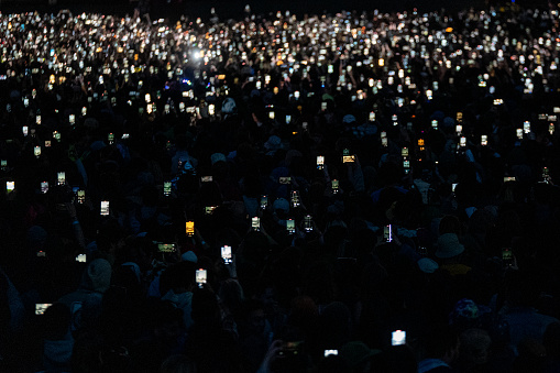 Concert goers pointing their cell phones to the stage of a concert in the dark,