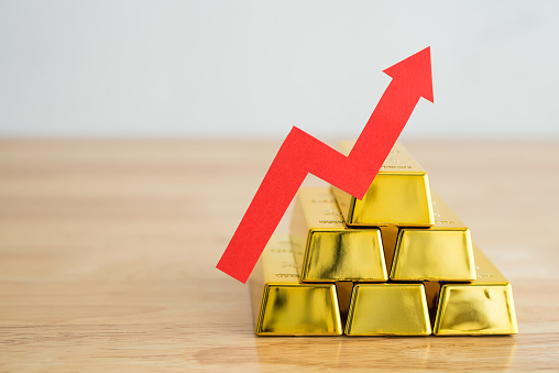 Gold bars stacks and red graph chart growing up on wooden background copy space. Gold price increase in commodity trading bull market investment concept. Gold is store of value in recession crisis.