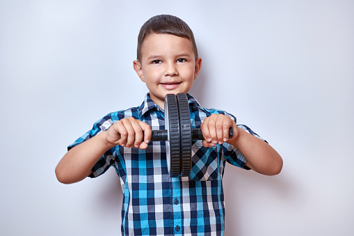 A little boy is standing and holding a gymnastic wheel in his hands. Fitness classes.