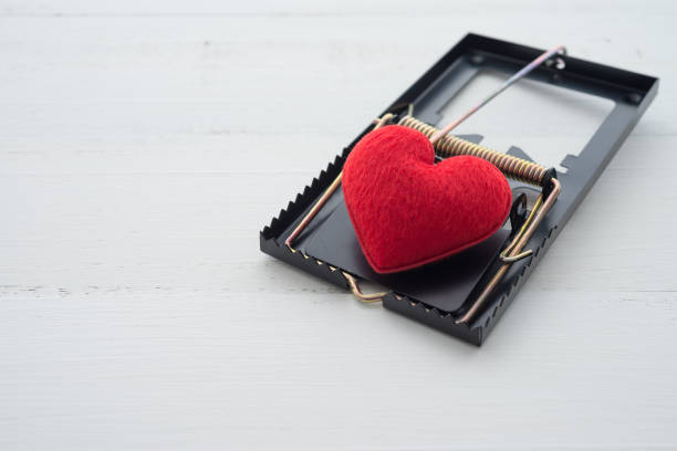 istock Red heart in a mousetrap on white wooden background. 1617942773