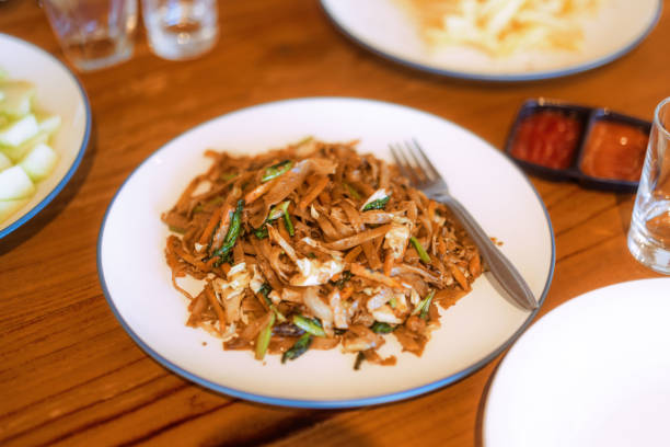 Top view of spicy fried instant noodles topped with fried onions and vegetables in a white plate on a wooden table. Spicy variant of fast food noodles
