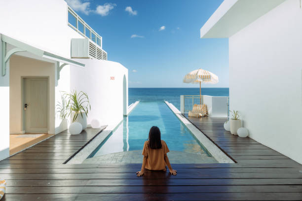 Beautiful Asian Woman Sitting at the Edge of Infinity Pool in A Luxury Beach Villa stock photo