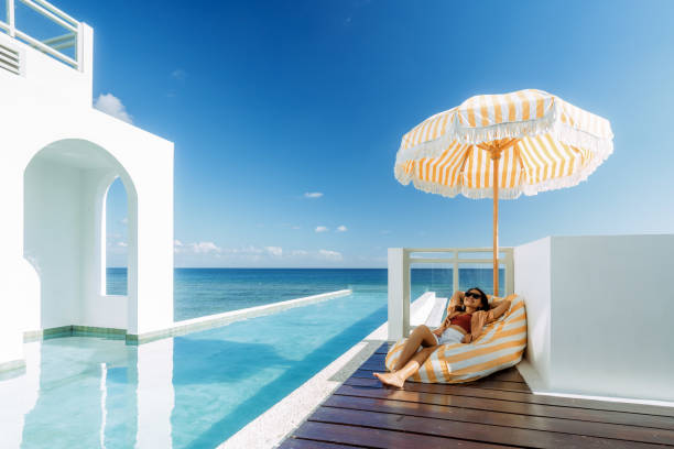 Beautiful Indonesian Relaxing Under Yellow Stripped Umbrella At the Infinity Pool Side Beach house luxury villa in Lemo-Lemo beach South Sulawesi Indonesia travel hotel accommodations stock pictures, royalty-free photos & images