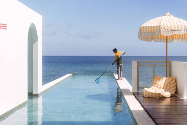Housekeeping Staff Cleaning Up Infinity Pool Beach Side Property stock photo
