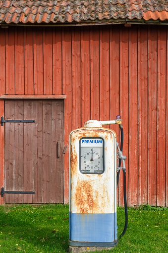 Old rusty gas pump by a red barn