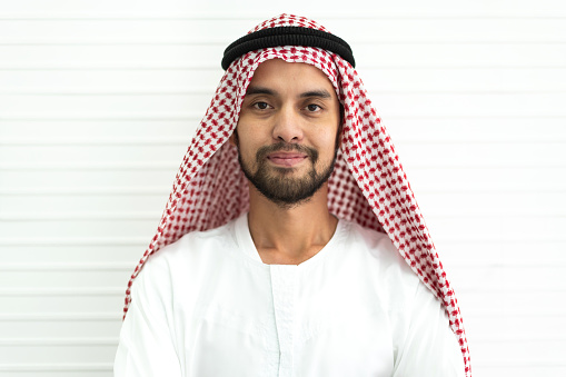 Portrait of happy smiling handsome middle eastern arab man in traditional clothing standing on white wall background