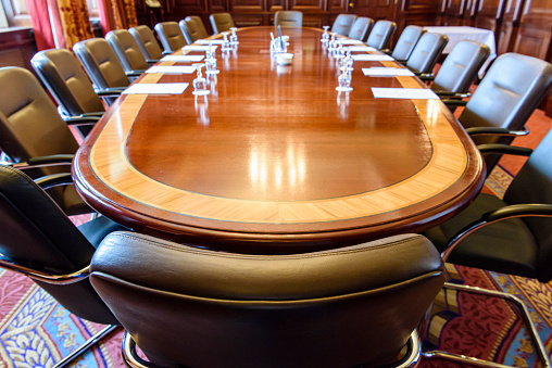 Large wooden table in a board room with wood panelling, set up for a meeting