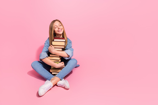 Photo of lovely dreamy satisfied girl wear stylish denim clothes hug pile stack books sit empty space isolated on pink color background.