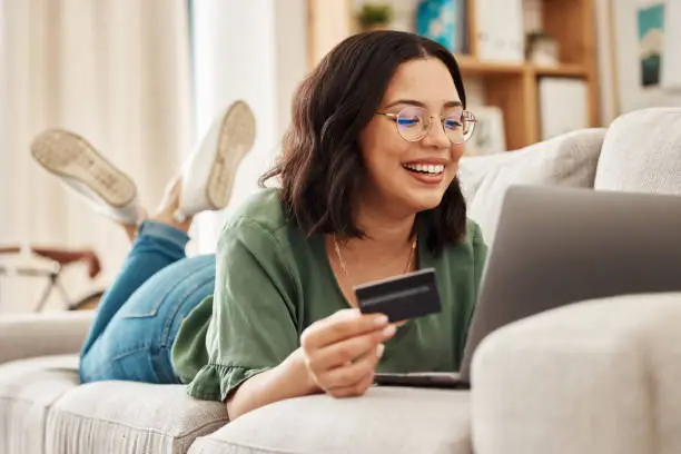 Photo of Relax, laptop and credit card, happy woman on couch in living room for internet banking in home for online shopping. Ecommerce payment, smile and cashback, girl on sofa with computer and website sale