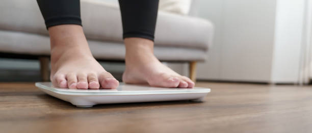 istock Fat diet and scale feet standing on electronic scales for weight control. Measurement instrument in kilogram for a diet control. 1618141377